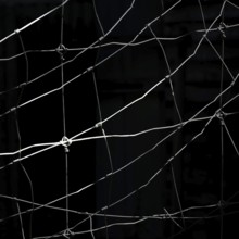 Worn netting stretches across a dark backdrop, showcasing intricate patterns and textures. The play