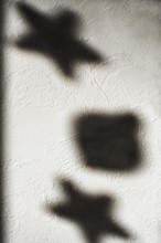 Shapes of stars and a square cast shadows on a textured white wall, illuminated by gentle light.