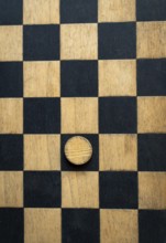 A close-up view of a checkerboard made of black and natural wood squares featuring one wooden piece