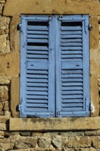 Bright blue shutters adorn the weathered stone wall of a traditional building in a picturesque