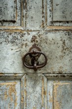 A close-up of a weathered wooden door surface reveals peeling paint and a vintage metal knocker.