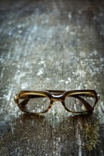 Vintage eyeglasses are displayed on a weathered wooden surface, illuminated by soft, warm light