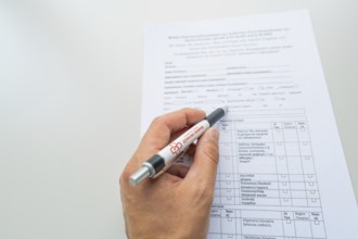 Hand holding a pen while filling out a form on the desk, Care Connect, vaccination kiosk for