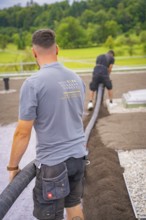Two construction workers lay a hose on a roof with a view of the surrounding nature, roof greening,