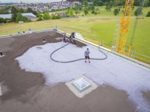 Workers attaching hoses to a roof next to an open field, roof greening, house construction, climate