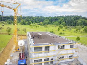 A building under construction with a crane and surrounding landscape, green roof, house