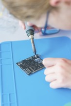 Person soldering on a circuit board lying on a blue base