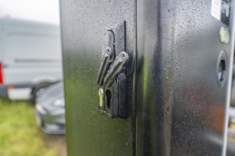 Security lock on a rain-soaked, black housing next to a parked car, installation of a charging