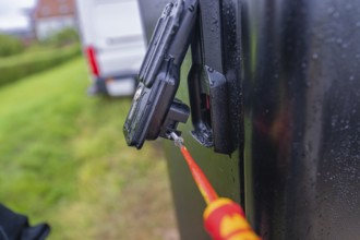 Screwdriver in use on a wet, black housing outdoors, assembly of a charging station for electric