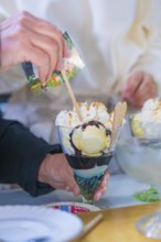 A delicious ice cream sundae with cream and waffle is held by a hand, chocolate sauce visible,