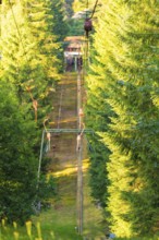 A ski lift moves quietly through a sunny forest surrounded by green trees, Retro Freizeitpark