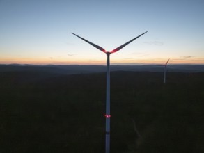 A wind turbine in front of a colourful evening sky with the silhouette in the darkness,