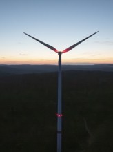 Wind turbine in front of a colourful sunset on the horizon. The sky glows in blue, red and orange,