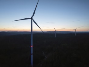 Several wind turbines on the horizon during a sunset, the sky is coloured in warm tones,