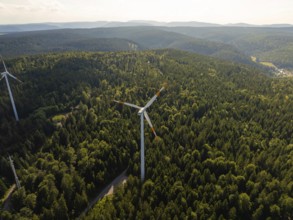 A wind turbine in the middle of a vast green forest under a blue sky in daylight, Simmersfeld,