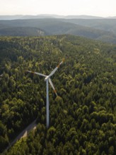 Single wind turbine surrounded by dense forest and green hills under a clear sky, Simmersfeld,
