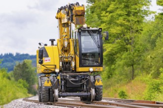 Large yellow construction machine on rails, surrounded by trees and greenery, grinding work on the