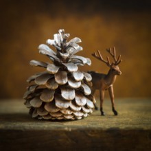 A charming deer figurine stands next to a large pine cone, evoking a cozy winter ambiance. This
