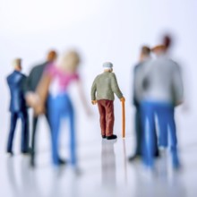 A group of diverse individuals stands behind an elderly man with a cane, who is walking forward,