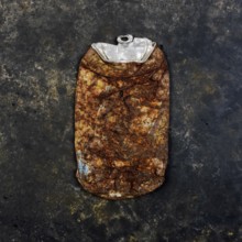 A rusty beverage can rests on a dark, textured concrete surface, highlighting urban litter and its