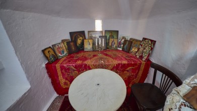 A table with red blankets and several icons flanked by candles in a small room, chapel, church,