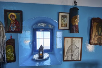 Blue painted wall with various religious pictures around a small window, chapel, church, Agios