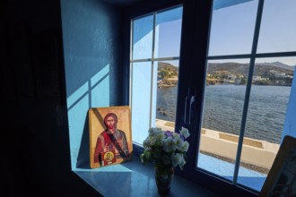 Icon on a windowsill overlooking the sea, surrounded by blue light and a bouquet of flowers,