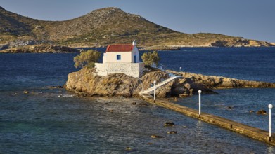 Whitewashed chapel on island, accessible via footbridge, surrounded by calm blue water, chapel,