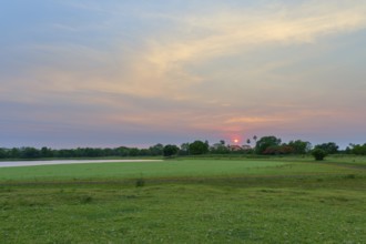 An idyllic landscape with a lake surrounded by trees and a warm morning sky at sunrise, Fazenda