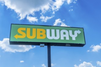 Green and yellow sandwich restaurant sign with white arrow pointing towards restaurant entrance