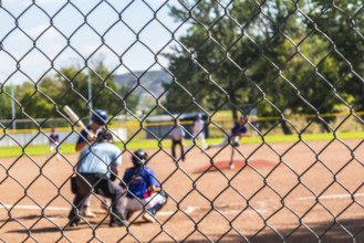 Blurred baseball players competing in a youth game, seen through a chain link fence, showcasing the