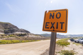 Bright orange no exit sign stands beside a dirt road leading into the arid badlands of drumheller,