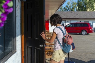 Female tourist with a backpack and rolling suitcase opening the door to a motel room after a long