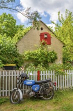 Blue motorcycle from the GDR brand Simson stands in front of an old house, village of Carwitz,