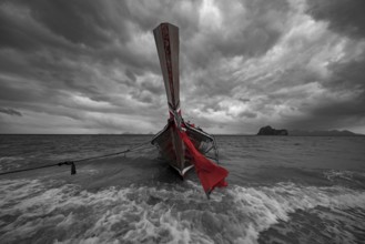 Longtail boat on the beach with dark rain clouds behind it, Koh Ngai island, Andaman Sea, Satun