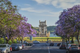 Scenic view of Belem Tower in Lisbon, Portugal, seen over a street with blooming purple jacaranda
