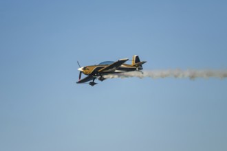 Golden stunt aerobatic plane performing stunts in blue sky with smoke trail. Concept of speed,