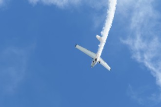 Stunt aerobatic plane performing stunts in blue sky with smoke trail. Concept of speed, difficulty,
