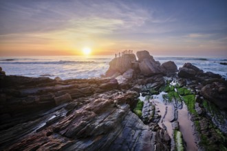 Scenic rock formation at Praia da Santa Cruz, Portugal, with ocean waves and vibrant sunset sky