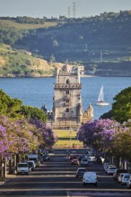 Scenic view of Belem Tower in Lisbon, Portugal, seen over a street with blooming purple jacaranda