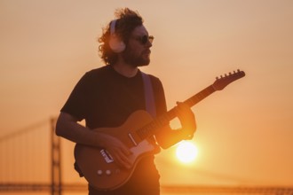 Hipster street musician in black playing electric guitar in street outdoors on sunset
