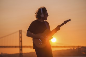 Hipster street musician in black playing electric guitar in street outdoors on sunset with lens