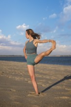 Woman yoga practice at the beach in Utthita Hasta Padangusthasana Extended Hand-to-Big-Toe Pose