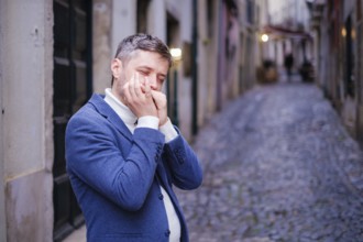 Man musician in a blue blazer and white sweater playing blues on a harmonica with eyes closed,