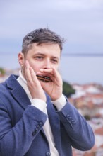 Man musician in a blue blazer and white sweater playing blues on a harmonica with eyes closed,