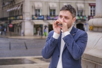 Man musician in a blue blazer and white sweater playing blues on a harmonica with eyes closed,