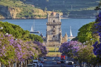 Scenic view of Belem Tower surrounded by blooming jacaranda trees, with sailboats on the Tagus