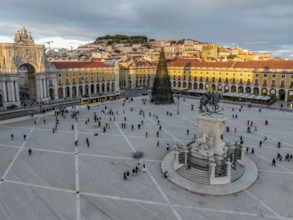 The scenic Praca do Comercio in Lisbon showcases a Christmas tree against the sunset sky,