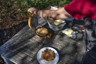 Preparation of waffles with a waffle iron on an outdoor garden table, Othenstorf,