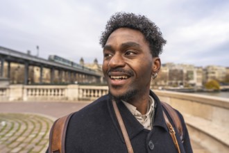 Happy black man smiling and looking away while strolling across paris bir hakeim bridge with a